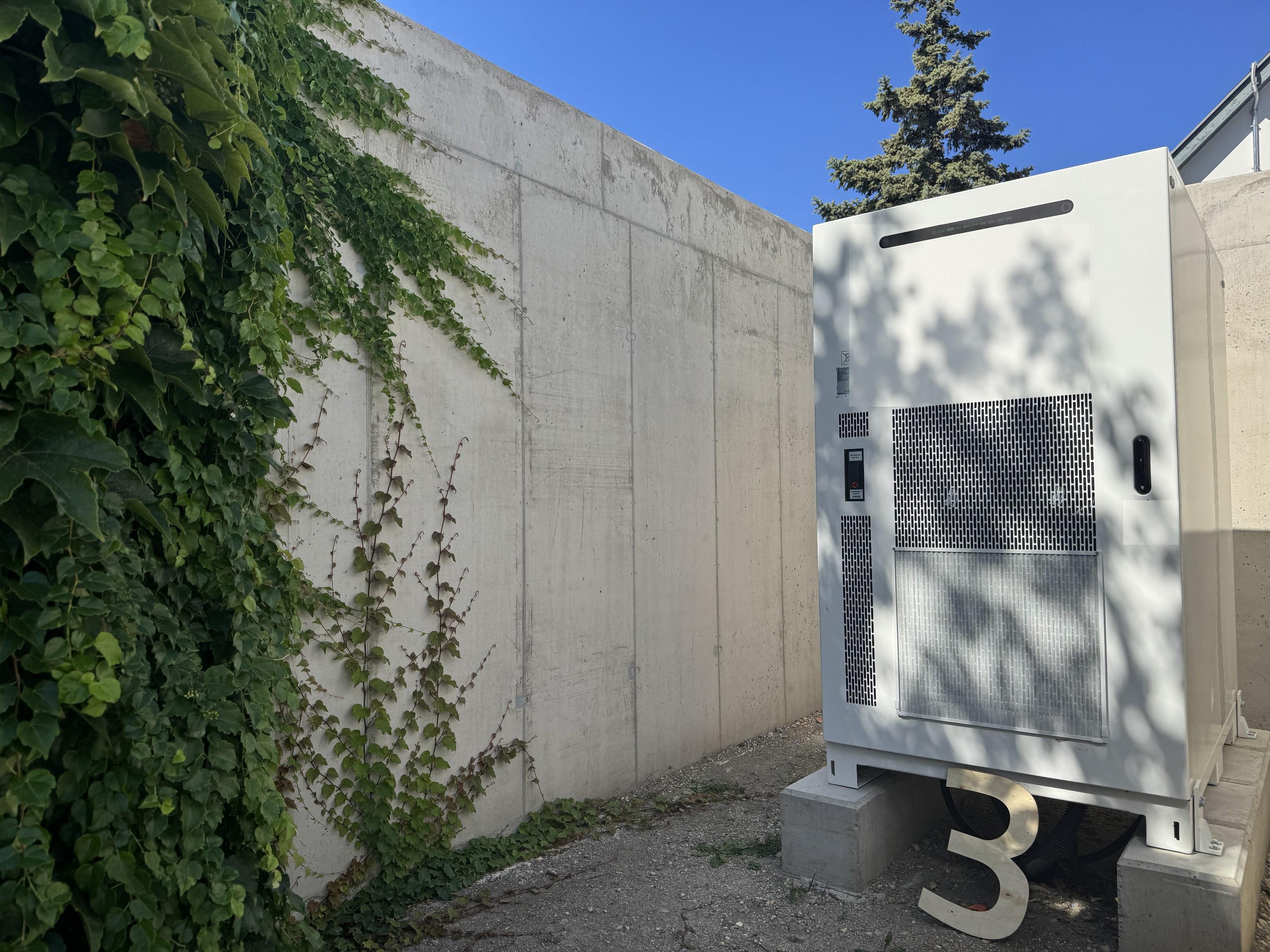 © Dachgold e.U. Weißer Batterieschrank im Freien, davor eine hölzerne Ziffer 3